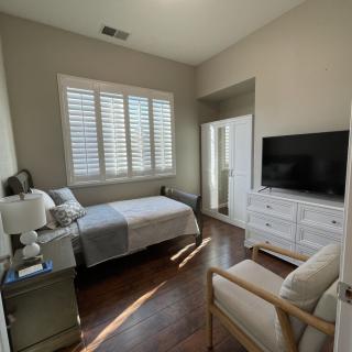 A well-lit bedroom with a bed, dresser, and TV.