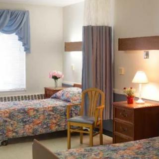 A shared room in a healthcare facility with two beds, a curtain for privacy, and bedside furniture.