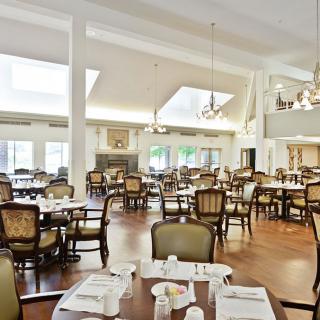 An elegant dining room with multiple tables and chairs, featuring chandeliers overhead.