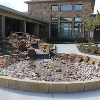 A beautifully designed outdoor area featuring a stone fountain surrounded by landscaping.