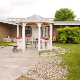A white gazebo with seating stands on a concrete patio, surrounded by a well-kept garden and lawn.