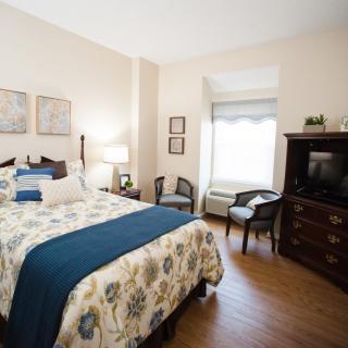 A cozy bedroom with a floral bedspread, wooden furniture, and soft lighting.
