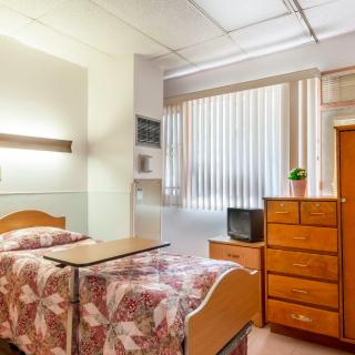 A hospital room with a single bed, wooden furniture, and a television.