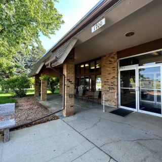 A building entrance with glass doors and a brick facade, surrounded by trees and a sidewalk.