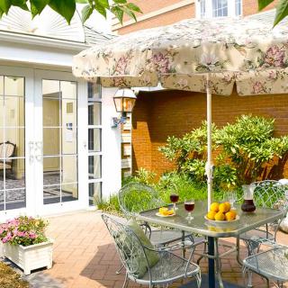 A sunny patio setup with a table and chairs under a floral umbrella, surrounded by plants.