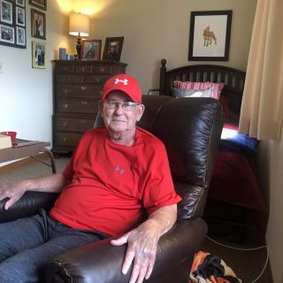 A man in a red shirt and cap sits comfortably in a chair in a living room.