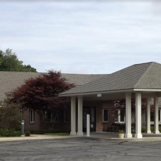 A building with a columned entrance and a parking lot in front, surrounded by trees.