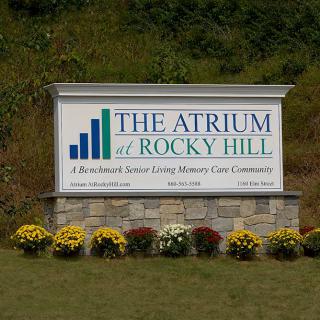 A sign for The Atrium at Rocky Hill, a senior living and memory care community, surrounded by flowers.