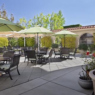 A sunny outdoor patio with tables, chairs, umbrellas, and potted plants.