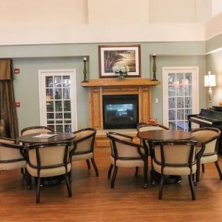 A cozy living room with tables and chairs arranged around a fireplace, complemented by a piano for an elegant touch.