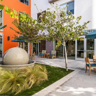 A modern courtyard with outdoor seating and a spherical art installation surrounded by greenery.