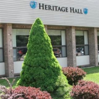 A landscaped area with a trimmed bush in front of the Heritage Hall building.