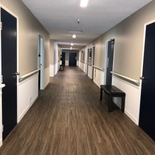 A long, well-lit corridor with multiple doors and a small seating area.