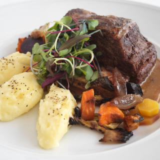 A plate of beef with mashed potatoes, roasted vegetables, and garnish.