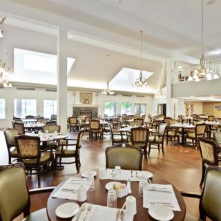 A spacious dining room with elegantly arranged tables and chairs, illuminated by natural daylight and chandeliers.