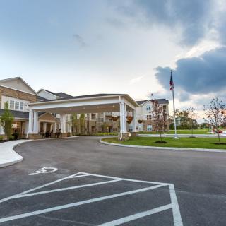 A large building with an entrance driveway and a flagpole in the parking lot under a cloudy sky.