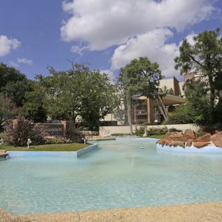 A serene outdoor pool surrounded by trees and buildings under a partly cloudy sky.