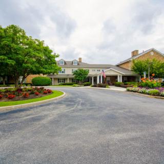A scenic view of a building entrance surrounded by landscaped gardens and trees under a cloudy sky.