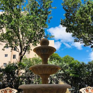 A serene fountain surrounded by lush greenery and a bright blue sky.