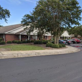 A quaint residential building surrounded by greenery and parked cars.