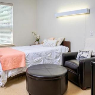 A neatly arranged bedroom with a bed, a black armchair, and a round ottoman.