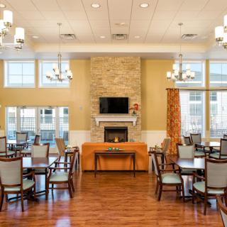 A spacious dining room interior with multiple tables and chairs, featuring a fireplace and elegant chandeliers.