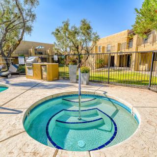 A hot tub in an outdoor pool area within a residential complex, surrounded by trees and a clear sky.
