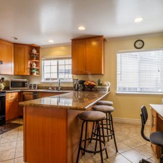 A modern kitchen with wooden cabinets, a granite countertop, bar stools, and various appliances.