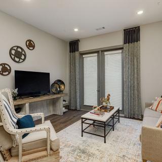 A cozy living room featuring a TV, sofa, armchair, and coffee table, with decorative items and curtains complementing the space.