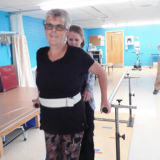 An elderly woman receiving assistance during physical therapy to improve her walking ability.