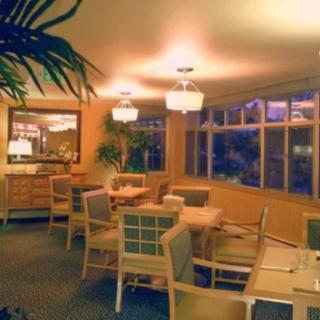 A cozy dining area with tables and chairs, warmly lit and featuring large windows.