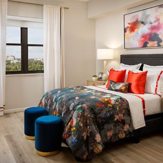 A stylishly decorated bedroom featuring a colorful bedspread, abstract artwork, and modern furniture with a view from the window.