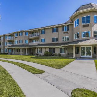 A three-story residential apartment building with a well-maintained lawn and pathways on a sunny day.