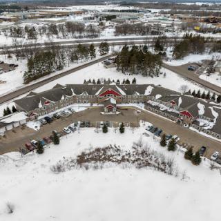 Aerial view of a snowy landscape featuring a building complex surrounded by parked cars and trees.