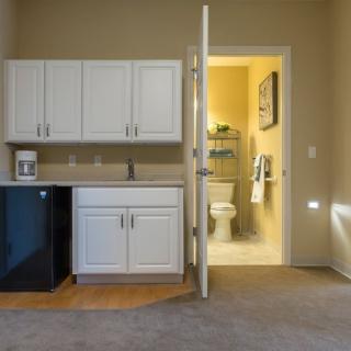 A compact kitchenette with white cabinets and an adjacent bathroom in a small apartment.