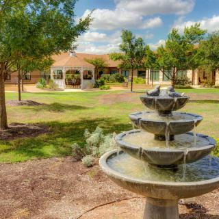 A serene garden features a tiered fountain and a gazebo surrounded by trees under a blue sky.