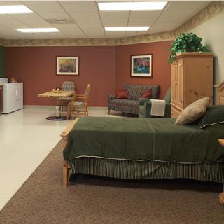 A cozy living space featuring a bed, sofa, dining table with chairs, and a refrigerator.