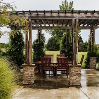 A picturesque outdoor seating area under a wooden pergola surrounded by lush greenery.