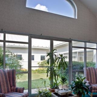 A cozy living room with large glass doors, featuring a variety of plants and comfortable seating.