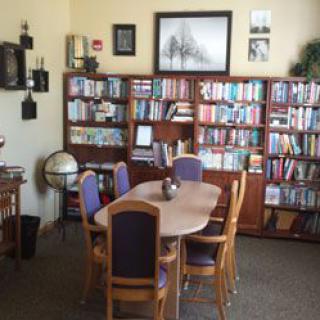 A cozy library with a wooden table and chairs surrounded by bookshelves filled with books, featuring a globe and wall art.
