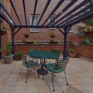 Outdoor patio with a pergola and green metal furniture surrounded by potted plants.