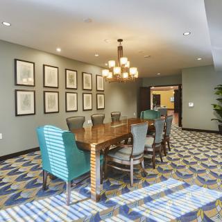 A modern conference room with a large wooden meeting table, elegant chandelier, and framed wall art.