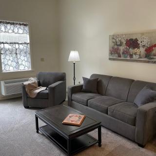 A cozy living room with a gray sofa and armchair, a coffee table, and decorative elements like a painting and lamp.