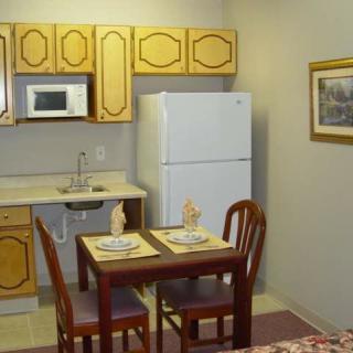 A small kitchen with a dining area, featuring wooden cabinets, a refrigerator, and a table set for two.