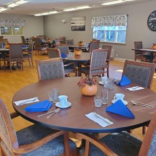 A well-arranged dining room with tables set for a meal, featuring blue napkins and autumn-themed decorations.