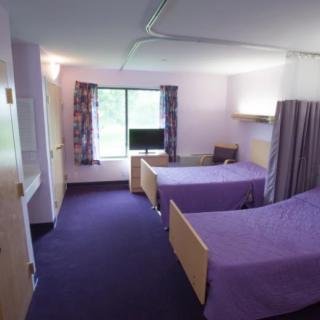 A hospital room with two beds and a small television near the window.