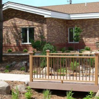 A brick house with a small wooden deck and landscaped garden in the front.