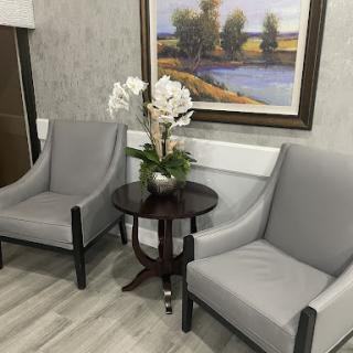 A cozy seating area featuring modern gray chairs, a decorative table with flowers, and a nature painting on the wall.