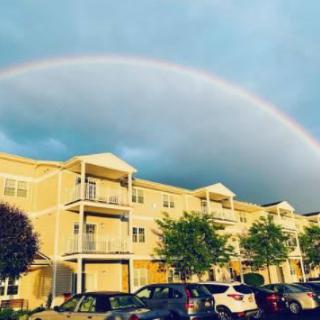 A vibrant rainbow arches over a row of apartment buildings under a stormy sky.