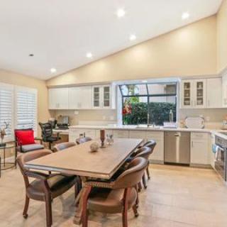 A modern kitchen with an open dining area featuring a wooden table and chairs, surrounded by white cabinets and bright indoor lighting.